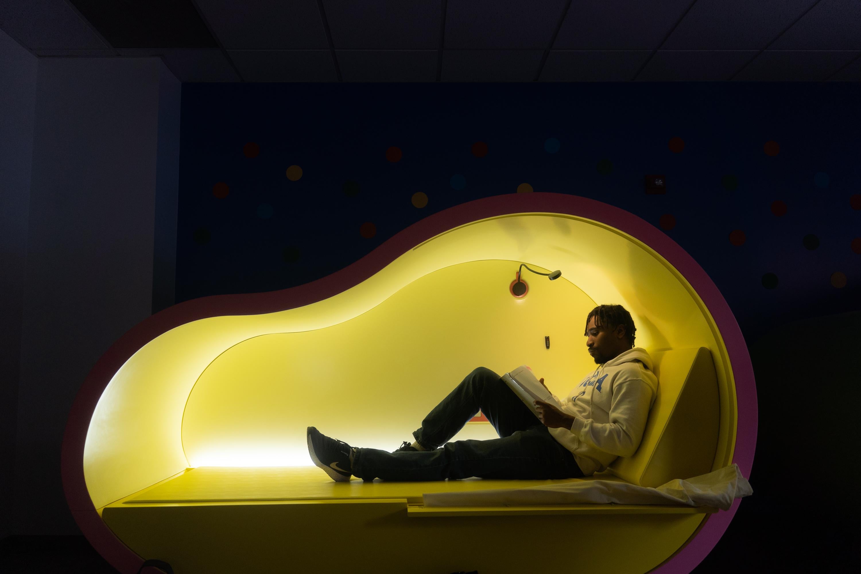 Photo of a student lounging in the pink BruinHub pod located in the Strathmore BruinHub. 